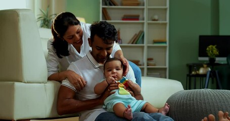Parents sitting with baby boy while sitting on floor near sofa in modern living room, showcasing Indian family bonding, love, parenting, parenthood, emotional care, happy lifestyle, and cozy moments