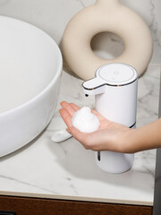 Woman using white automatic soap dispenser in bathroom