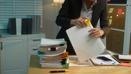 Business Asian woman in formal black suit thoughtfully reviews documents at her desk late at night, critical thinking, and commitment to meeting deadlines during late-night work hours.