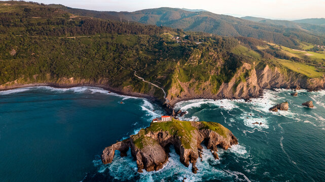 Impressive aerial shot of the historic hermitage of San Juan de Gaztelugatxe, on the Basque coast, with rugged cliffs, deep blue sea, and the iconic stone staircase leading to the chapel atop 