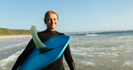 Mature woman posing with a single fin surfboard at the beach