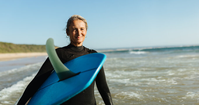 Mature woman posing with a single fin surfboard at the beach