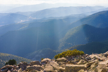 Landscape with majestic view from Carpathian peak with sunrays shining over endless green mountain ranges covered with coniferous forest and rocky slopes.