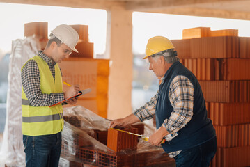 Construction workers measuring bricks and taking notes on building site