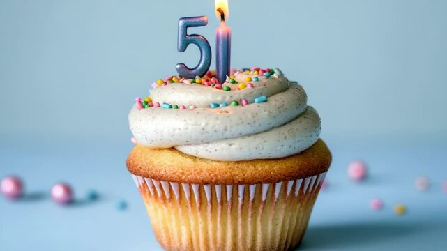 Celebratory cupcake with frosting and sprinkles, topped with a lit candle celebrating a 5th birthday.