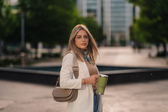 Businesswoman holding reusable coffee cup walking in urban city center