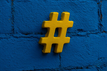 Bright yellow hashtag symbol against a vivid blue brick wall representing social media influence and connectivity in urban environments