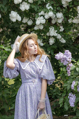 A beautiful young blonde woman, against a background of blooming lilacs, in a lilac vintage dress. A walk in the park.