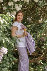 A beautiful young blonde woman, against a background of blooming lilacs, in a lilac trouser suit. Femininity and nature.