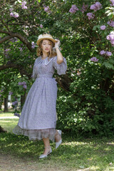 A beautiful young blonde woman, against a background of blooming lilacs, in a lilac vintage dress. A walk in the park.