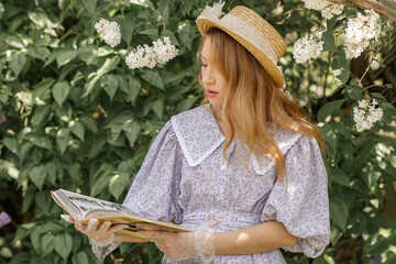 A beautiful young blonde woman, against a background of blooming lilacs, in a lilac vintage dress. A walk in the park.