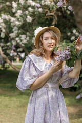 A beautiful young blonde woman, against a background of blooming lilacs, in a lilac vintage dress. A walk in the park.