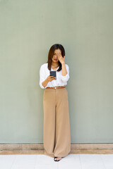 Fototapeta premium Full length portrait of woman standing in front of wall wearing business clothes using mobile phone