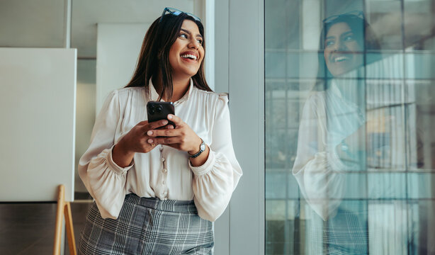 Confident businesswoman standing by the window smiling and reflecting success and positivity