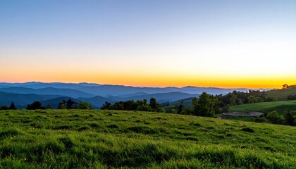 Obraz premium Rolling green hills at dusk, layered mountains under a pastel orange gradient sky