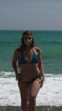 Woman Mask Beach Woman wearing tribal gold face mask and bikini standing on beach by ocean waves