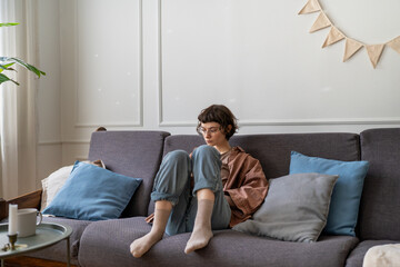 Tired upset young woman sitting sadly on couch at home, feeling anxious, stressed due to bullying...