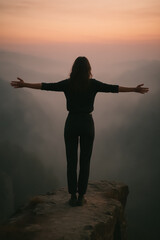 Woman standing on cliff with arms outstretched facing misty sunrise, silhouette. generative AI