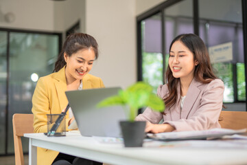 Obraz premium Two professional businesswomen are working on laptop computers sitting at desks in the office. Colleagues are happy and discussing the digital strategy of the Graph