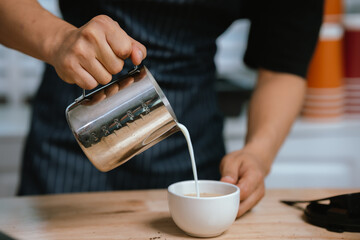 Barista pouring milk into cappuccino, creating latte art in cozy café setting, showcasing morning preparation, craftsmanship, and coffee culture indoors.
