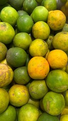 The image captures a large pile of oranges, displaying a mix of green and yellow-orange hues, suggesting varying stages of ripeness or different varieties