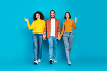 Obraz premium Group of three young friends walking together holding hands on a blue background showcasing diversity and friendship