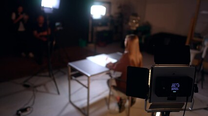 Soffit is illuminating a lady sitting at desk from behind. Footage in modern photo studio. - Powered by Adobe