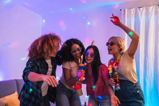 Group of cheerful young multiethnic friends singing karaoke and dancing together at a home party with disco lights