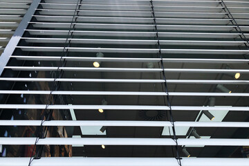A close-up, worm's-eye view of a modern building facade covered in grey external Venetian blinds, with interior lights visible through the slats, creating an abstract pattern