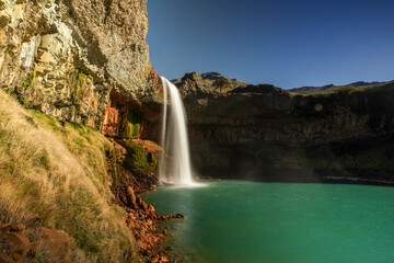 El Saltpo del Agrio waterfall cascading on turquoise water with colorful rock formations. Neuquen, Patagonia, Argentina