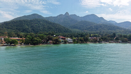 Turquoise water lapping against the sandy shore, hotels and resorts nestled among lush tropical vegetation, backed by majestic mountains under a bright blue sky in tioman island, malaysia