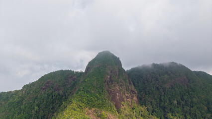 Low clouds enveloping the peaks of lush green mountains create a tranquil and mysterious atmosphere within a tropical rainforest, inviting exploration of its serene beauty