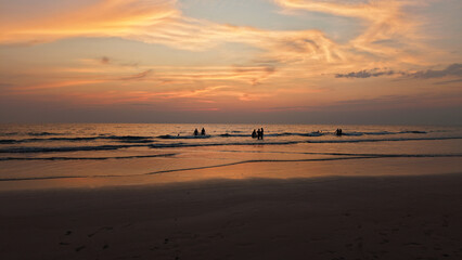 Tourists are enjoying the breathtaking view of a vibrant sunset over the ocean, creating a serene and memorable experience as gentle waves wash ashore