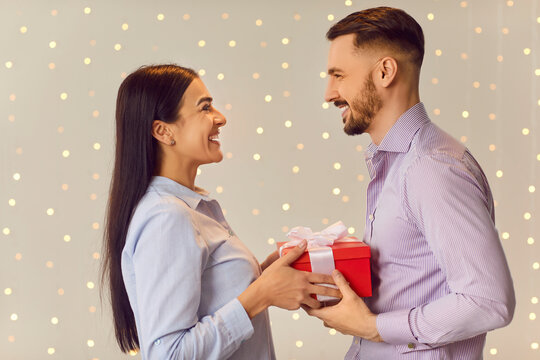Happy husband giving a gift box to his amazed young wife on Valentine Day, anniversary or birthday. The love, romance, and relationship are beautifully captured with tenderness and joy.