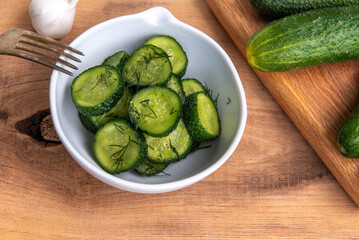 Organic cucumbers slices in a ceramic white bowl on a wooden table.