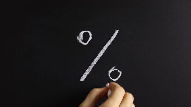 Closeup view of hand writing % on black chalkboard background. Concept of promotion sale announcement, advertising, discount, tax cut, tariffs increase, off season price decrease, special rate offer