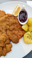 Wiener schnitzel with potato, lemon and cranberry jam on white porcelain plate