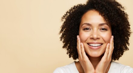 Smiling woman with curly hair touching face with both hands on beige background. Female showing healthy glowing skin and natural beauty confidence. Skincare wellness. Beauty product sale