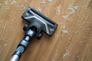 Vacuum cleaner nozzle picking up scattered rice grains from a wooden floor concept of cleaning,...