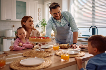 Happy father serving sweet pie to his family at dining table.