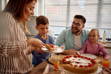 Happy woman serving strawberry tart for dessert during family meal in dining room.