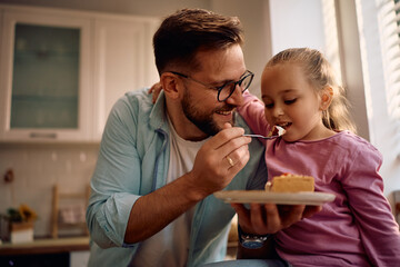 Happy father and daughter eating sweet pie in kitchen.