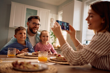 Happy family having fun while taking pictures at dining table.