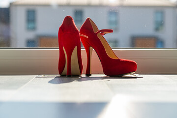 Red ladies pumps on the floor in front of a window