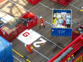 Workers expertly maneuver a heavy cargo container across a ships deck using ropes and precision. The scene showcases meticulous teamwork and efficient cargo handling procedures aboard a vessel.