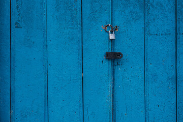Puerta de madera azul envejecida con candado metálico y cerradura oxidada