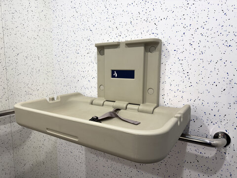 Open baby changing station with safety strap mounted on a public restroom wall. Practical hygienic facility designed for parents with infants in modern urban infrastructure
