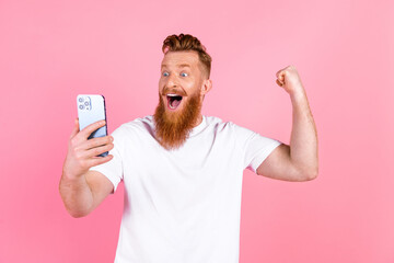 Excited young man with a beard celebrates success holding smartphone in front of a vibrant pink...