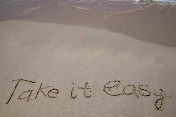 Words written in sand. The words TAKE IT EASY written in the sand on the beach.