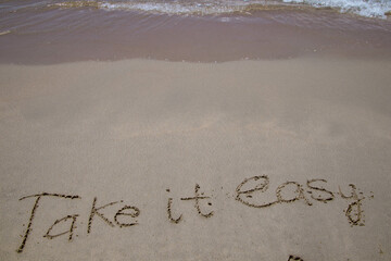 Words written in sand. The words TAKE IT EASY written in the sand on the beach.